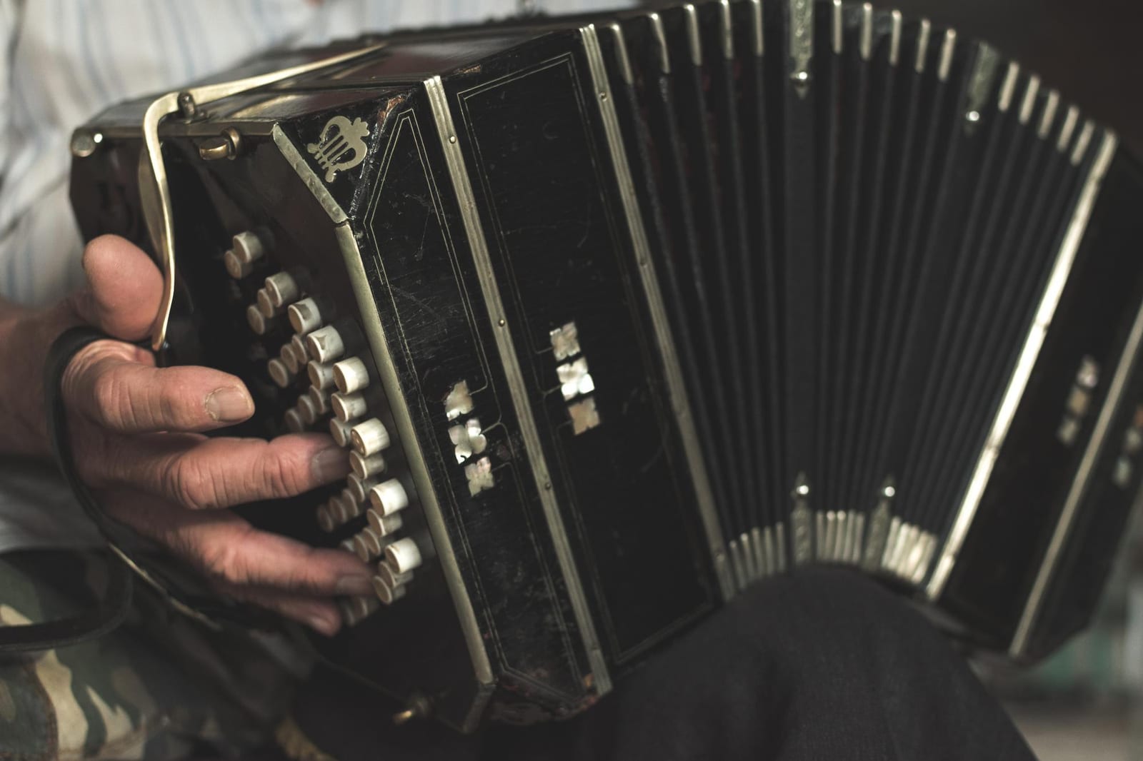 Acordeão dourado e preto com detalhes ornamentados apoiado no colo do músico